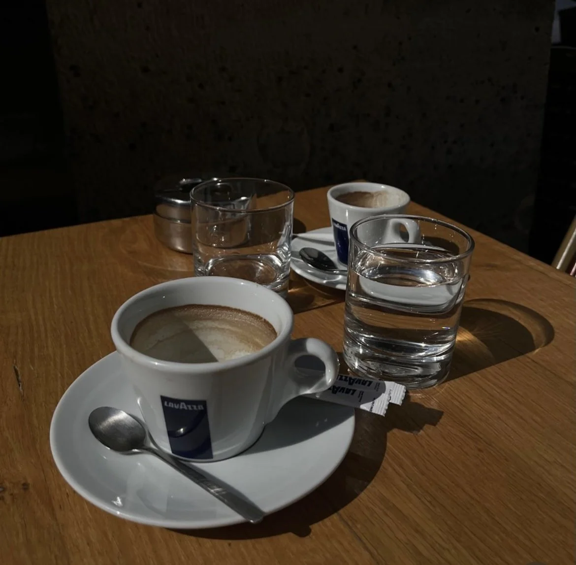 Deux tasses de café, deux verres d'eau, un sachet de sucre, une cuillère, un pot de sucre et une assiette avec une tasse de café. Pour inviter au premier contact avec Clara, à échanger et se rencontrer avant d'acter un accompagnement.
