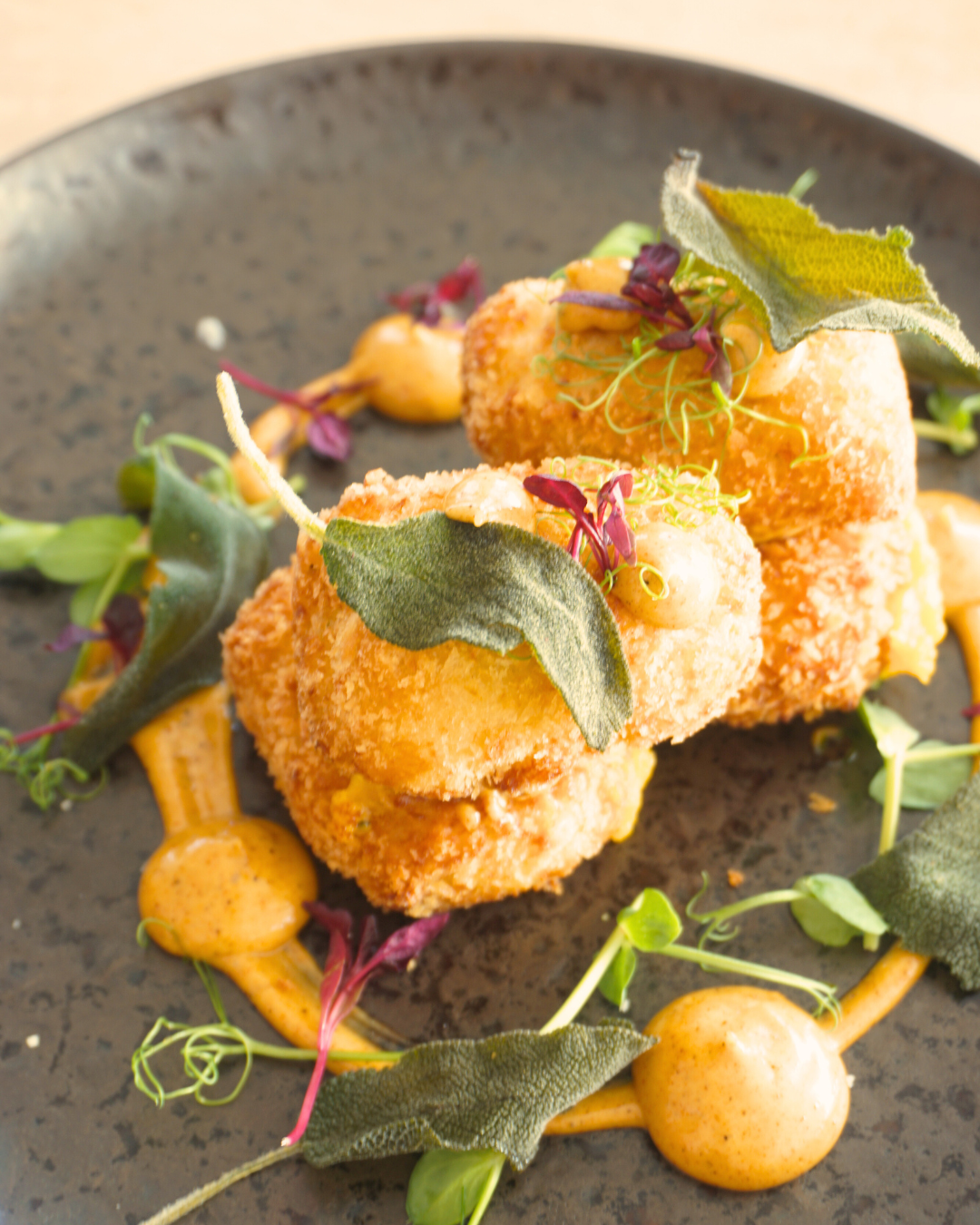 Grain Barge starter with microgreens and garnished with leaf herbs, served on a black plate with a dressing and additional garnishes surrounding it.