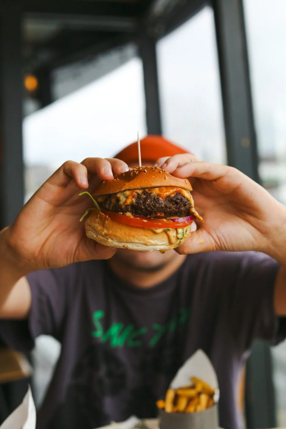 Person holding up a cheeseburger with lettuce, tomato, onion, and a beef patty in a bun, in Grain Barge restaurant.