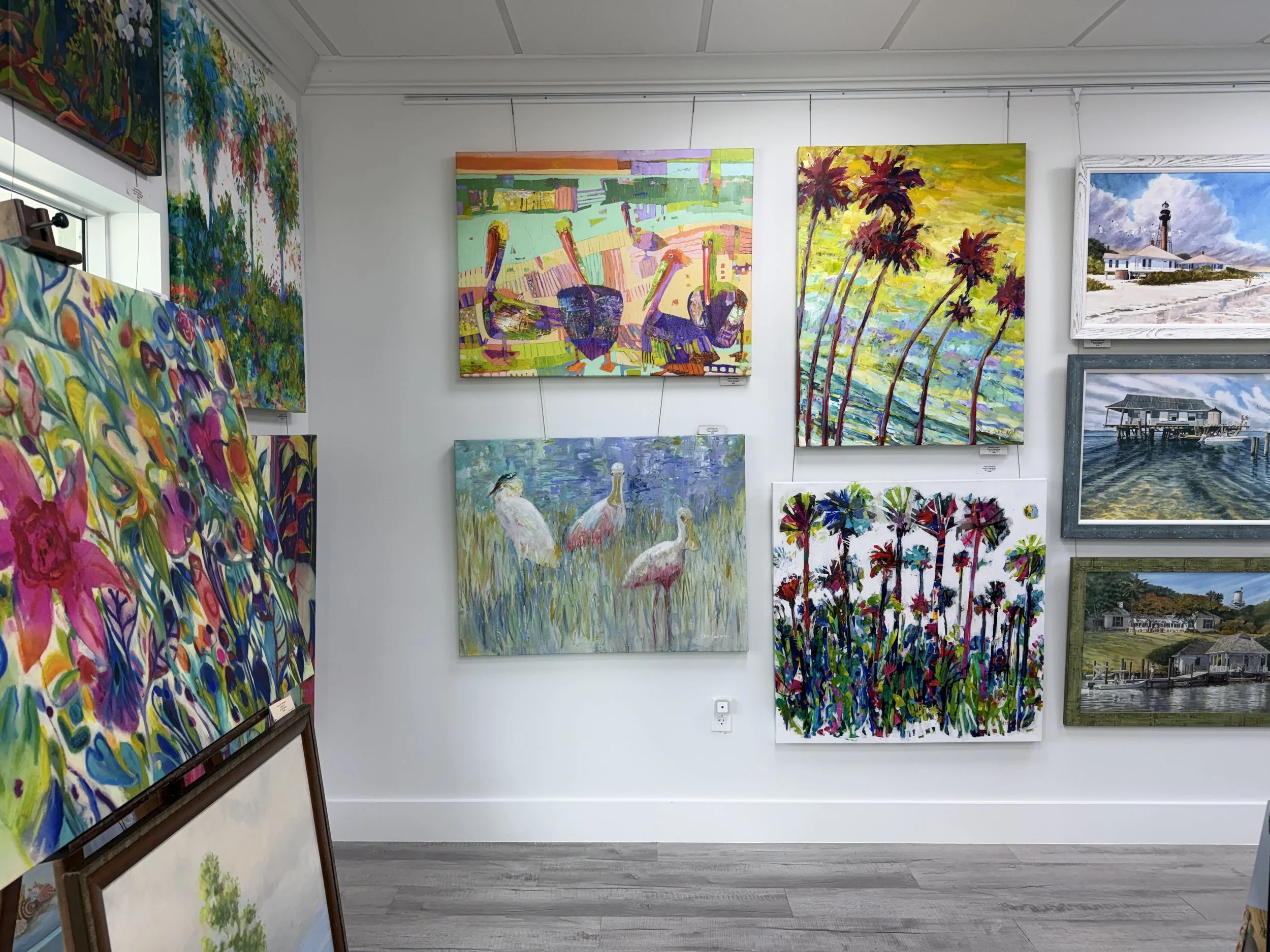 Gallery of colorful landscape and cityscape paintings in an art gallery, with vivid colors and diverse styles.