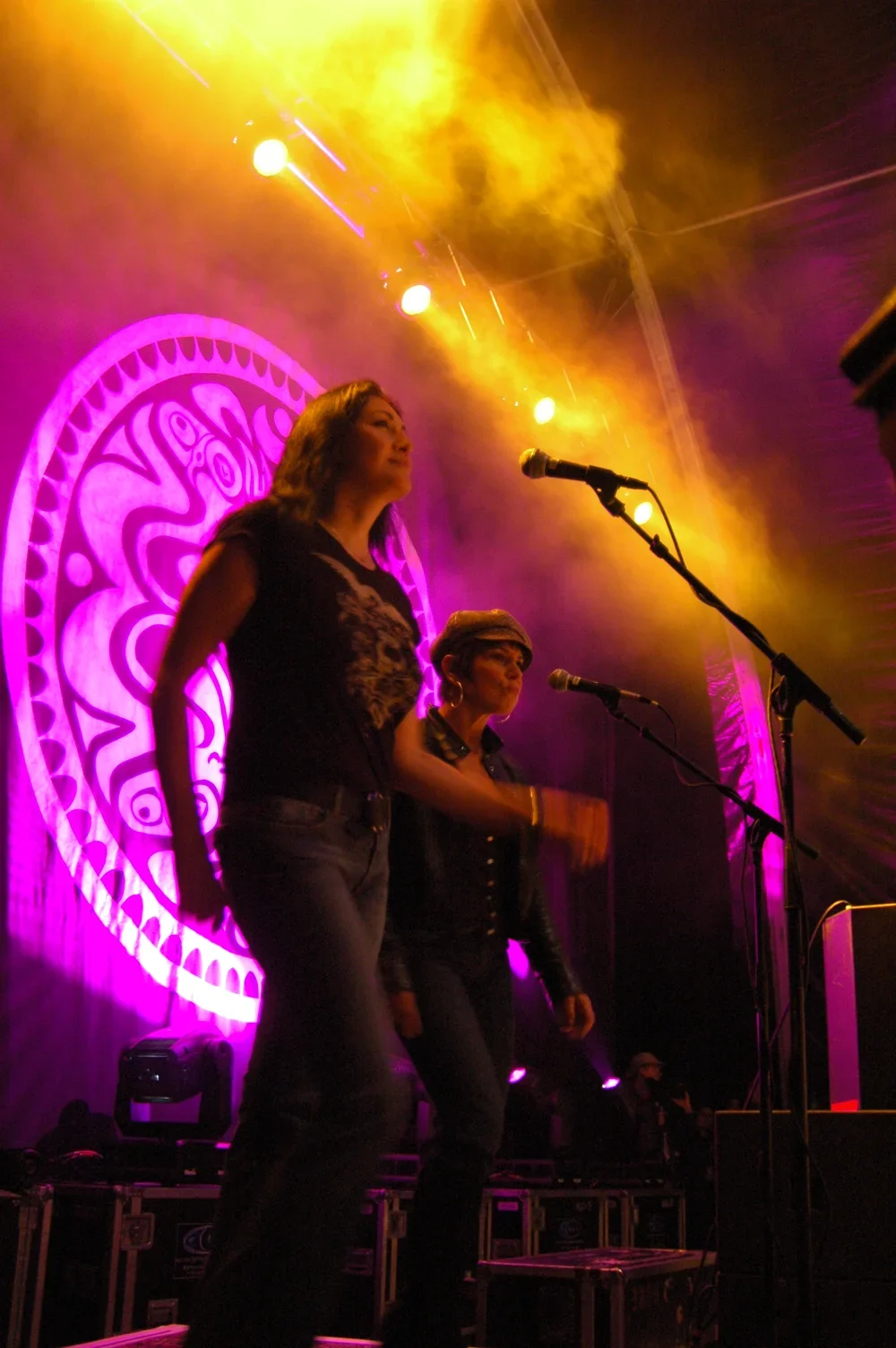 Women performing on stage with purple lighting and yellow smoke effects, standing in front of a decorative backdrop.