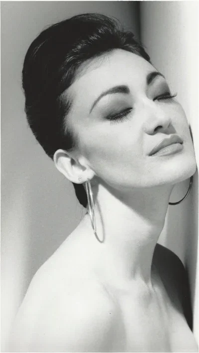 A black-and-white portrait of a woman with short dark hair, closed eyes, and a serene expression, wearing large hoop earrings.
