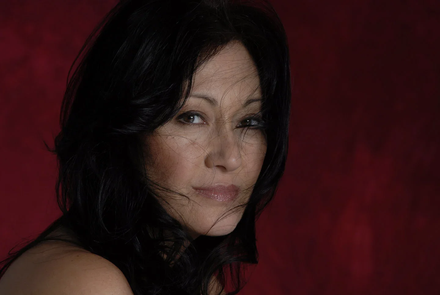 Close-up of a woman with black hair against a red background.