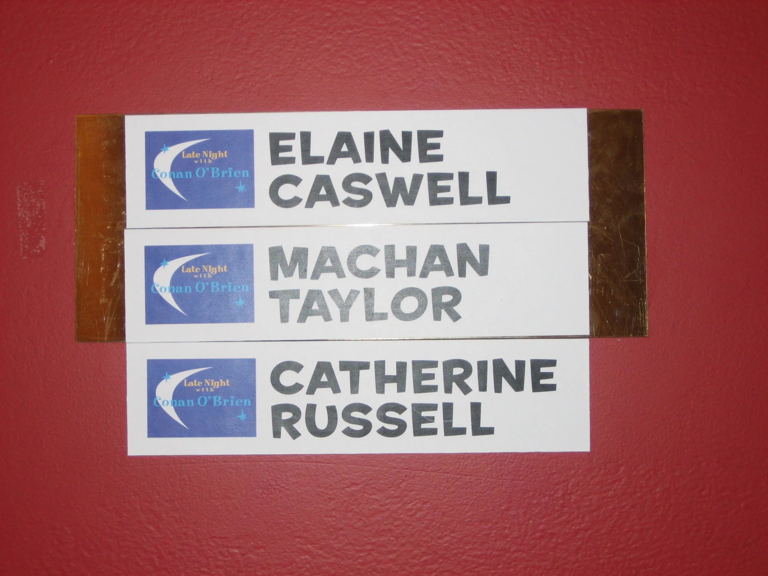 Name tags with the names Elaine Caswell, Mahan TAYLOR, Catherine Russell, and Russel, attached to a red wall with a blue logo in the top left corner that reads "Late Night with Conan O'Brien."
