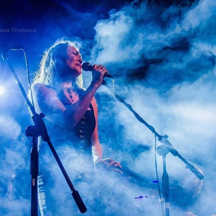 Female singer performing on stage with blue and white smoky lighting.