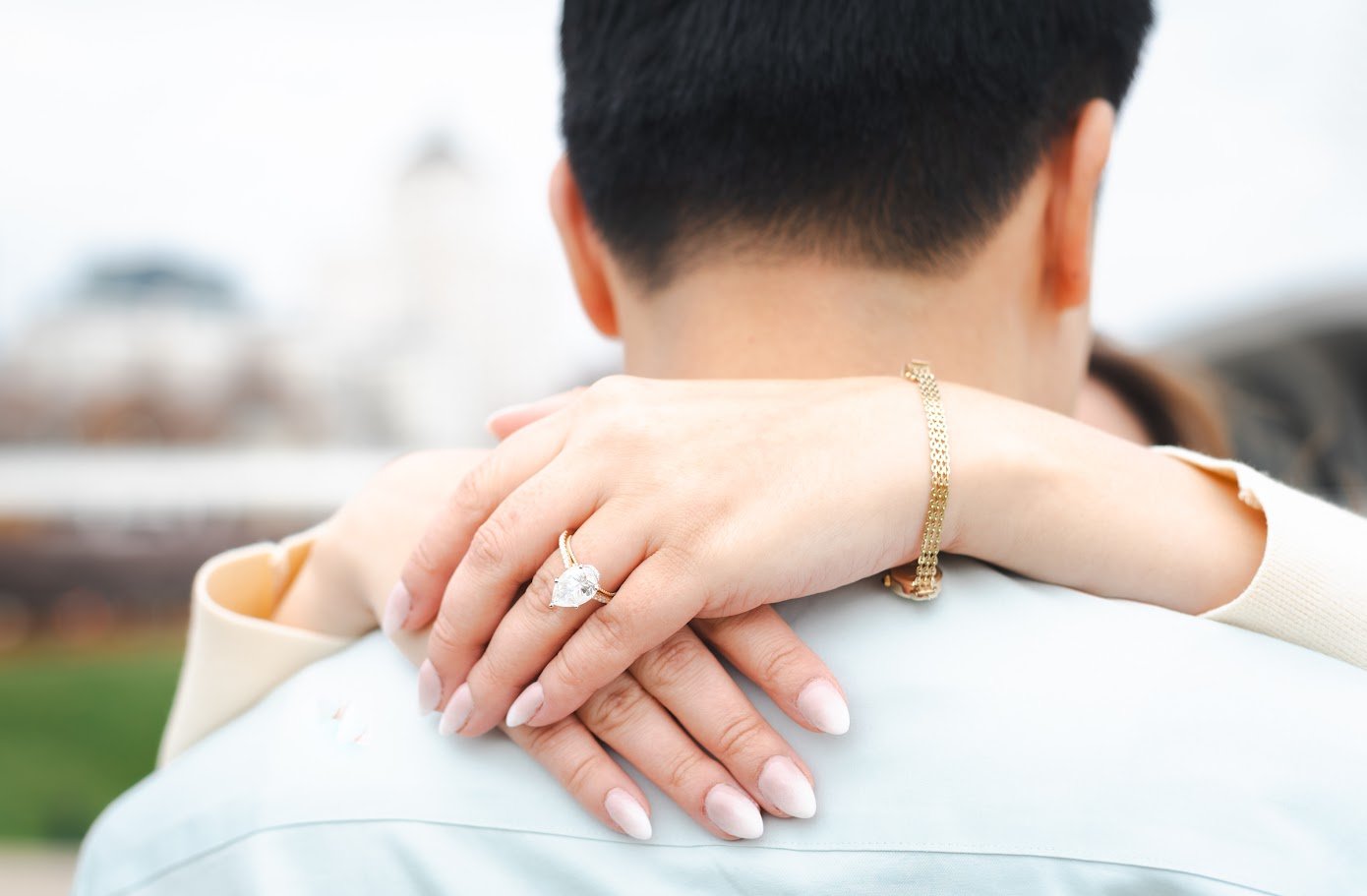 Close-up of a woman’s hand with an engagement ring on her finger, embracing a man’s neck from behind.