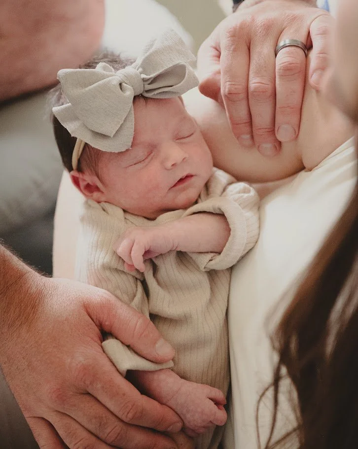 Newborn baby sleeping on mother’s chest, with hands gently holding the baby and a person with a wedding ring touching the mother’s face.