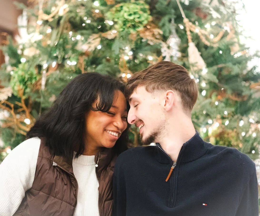 A couple noses touching with closed eyes in front of a decorated Christmas tree.