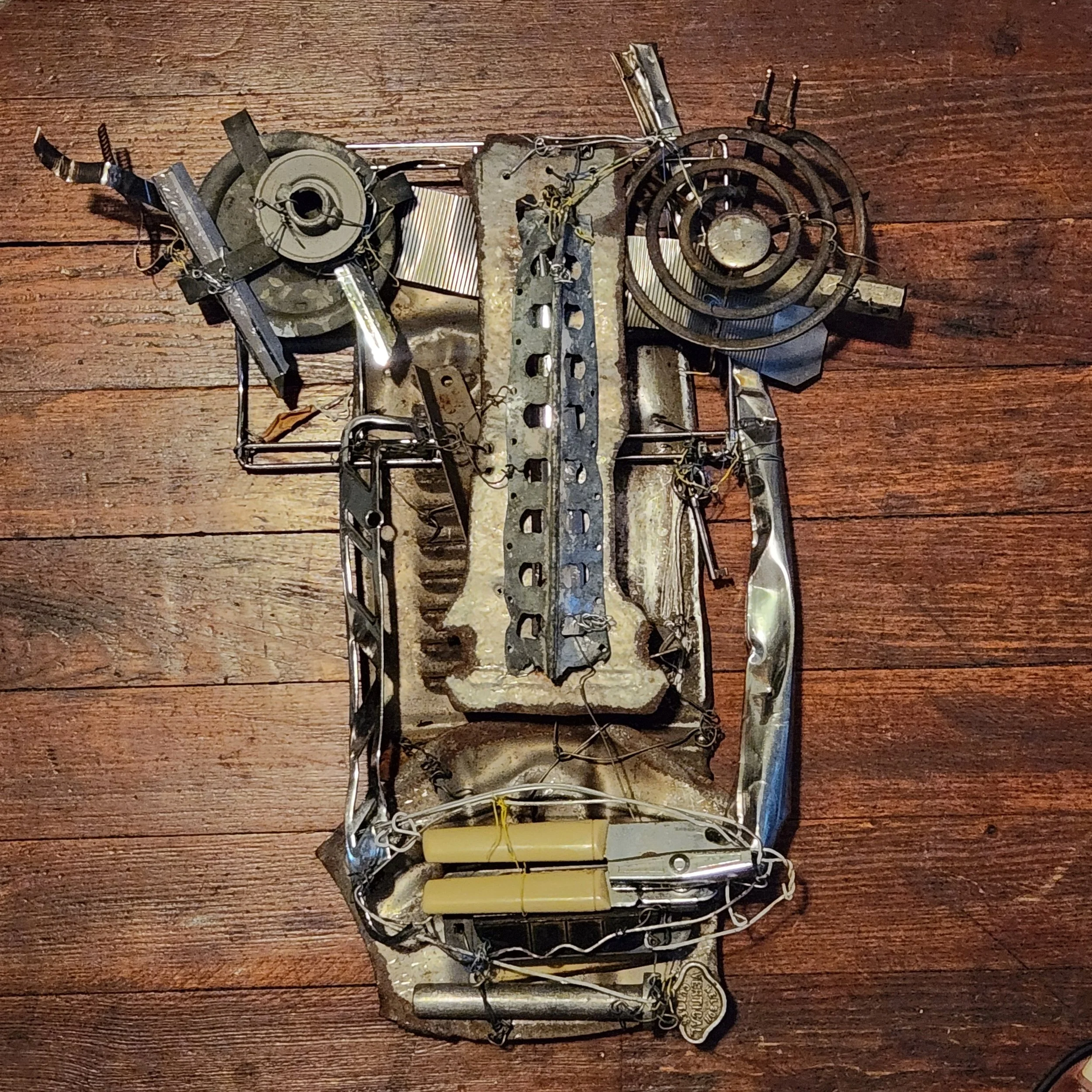 Found metal artwork by Karl A. McIntosh featuring electronic components, metal parts, wires, and circuitry arranged on a wooden surface.