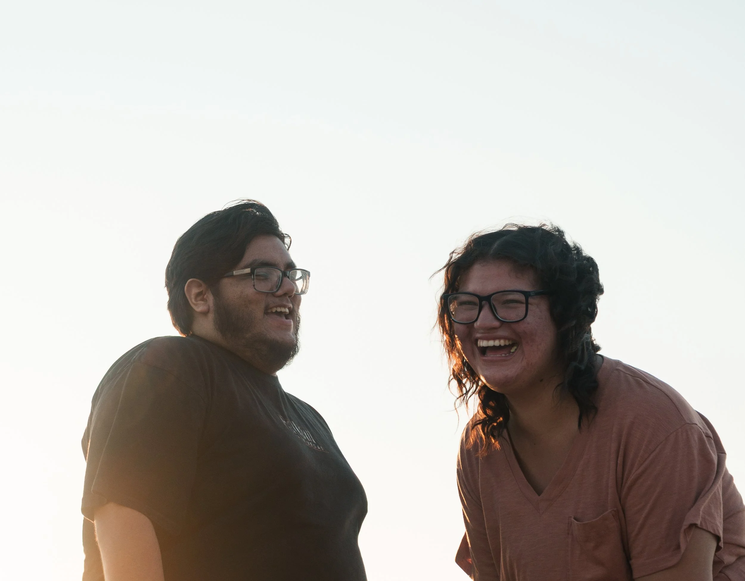 Couple standing close together and smiling, against a light, clear sky.