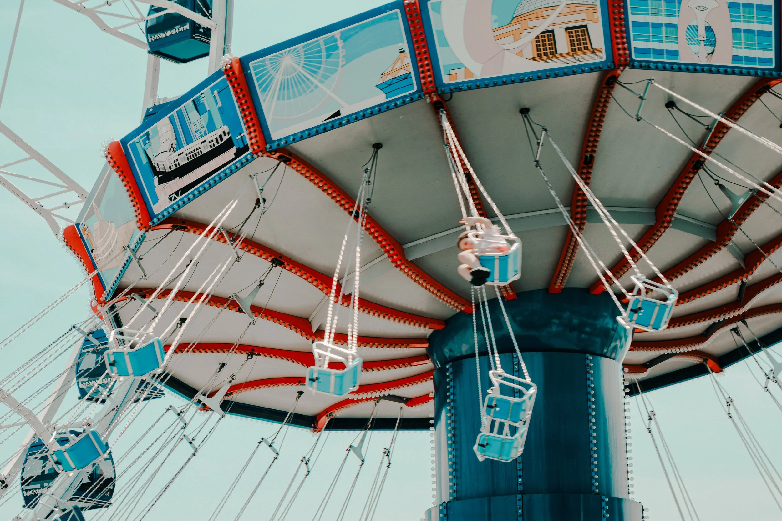 Close-up view of a vintage-style Ferris wheel with blue and white color scheme, featuring decorated gondolas and intricate structural details against a clear sky.