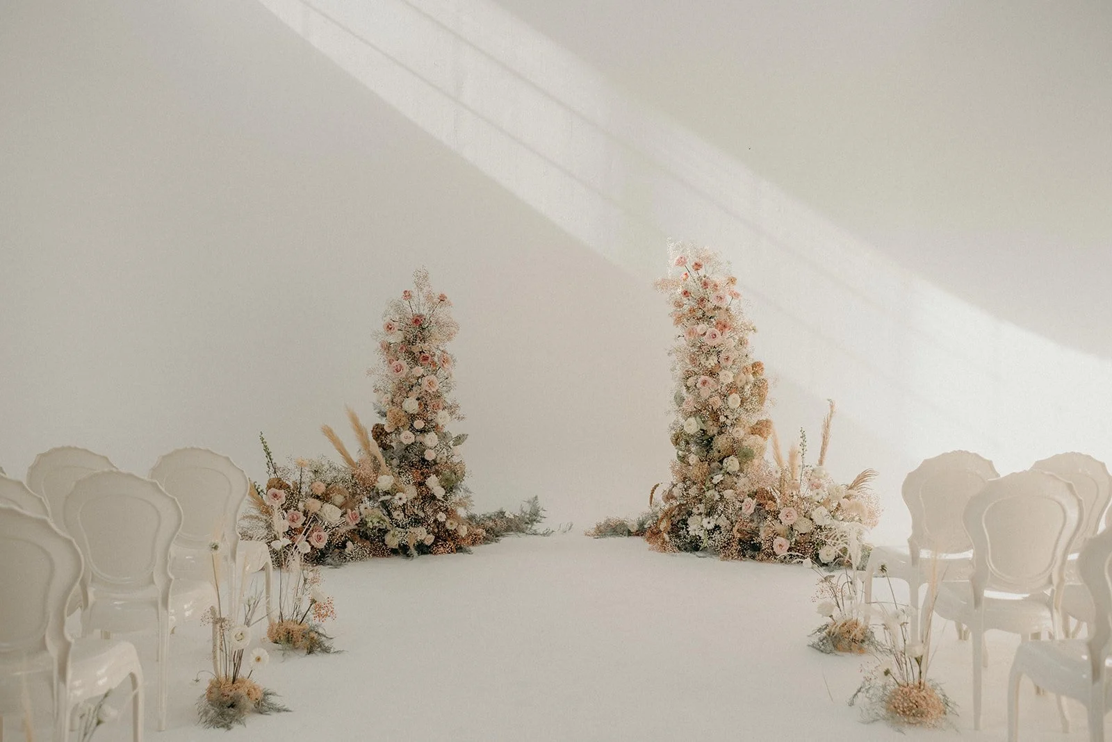 Elegant wedding ceremony setup with two large floral arrangements of pink and white flowers and white chairs on either side.