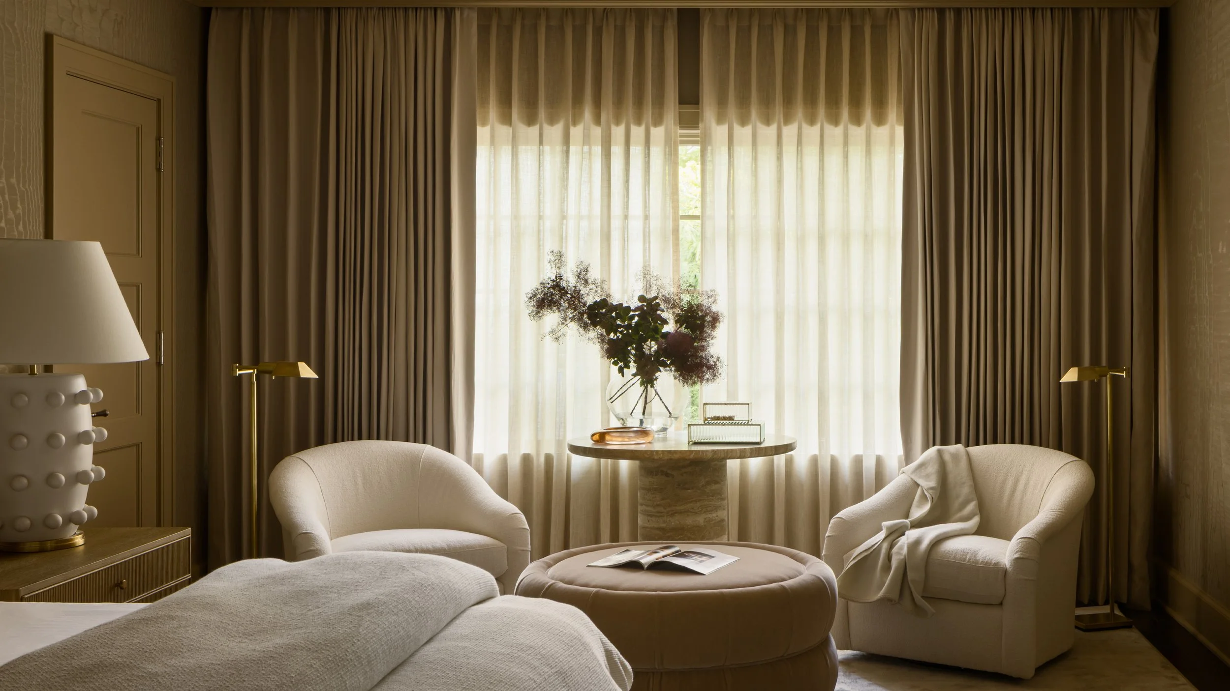 Living room with beige curtains, a glass vase with flowers on a small round table, a book, and cream-colored furniture.