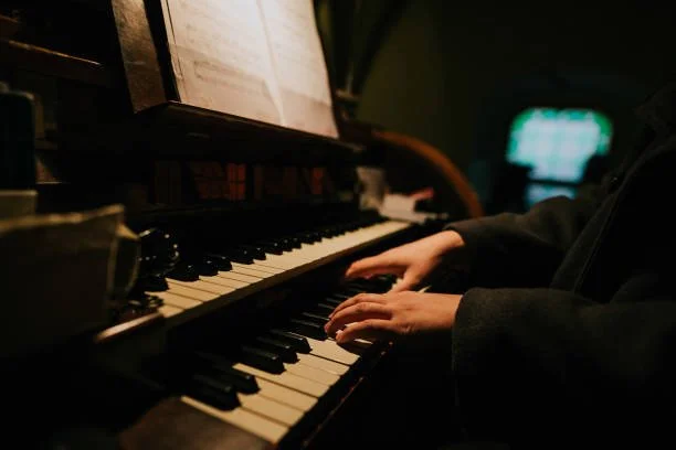 Person playing the piano in a dimly lit room with sheet music on the stand.