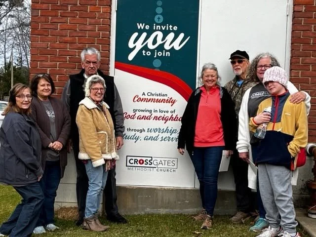 Group of people standing in front of church sign that invites community members to join and mentions worship, study, and service, affiliated with Crossgates Methodist Church.