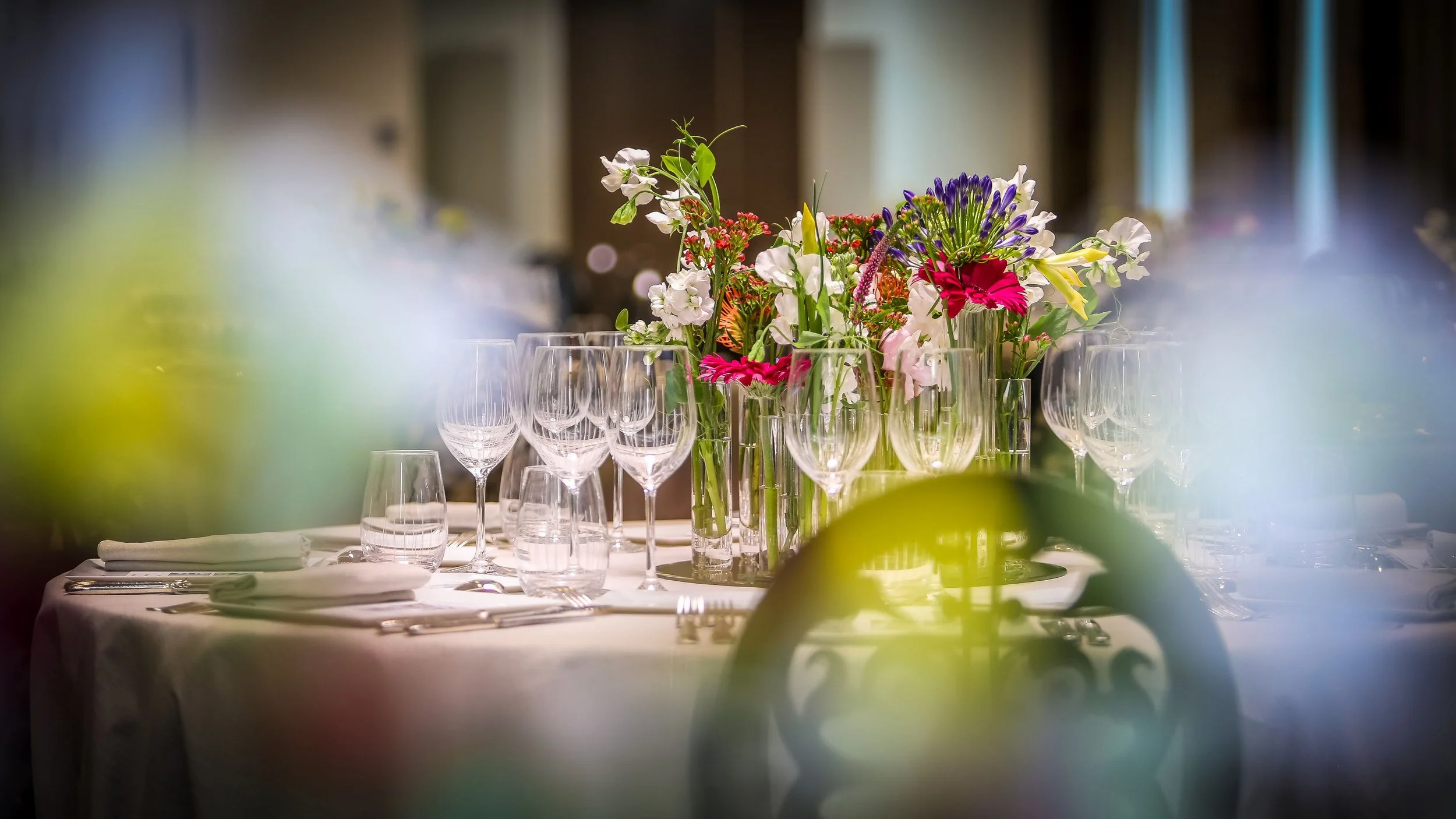 Une table élégante avec un centre de table de fleurs colorées, plusieurs verres à vin et de la vaisselle, prête pour un dîner ou une événement spécial.