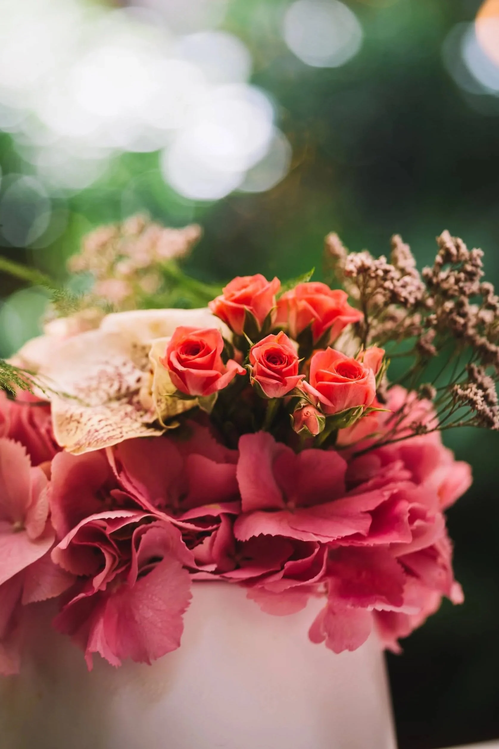 Un bouquet de fleurs roses avec d'autres petites fleurs violettes, sur un fond flou vert et lumineux.