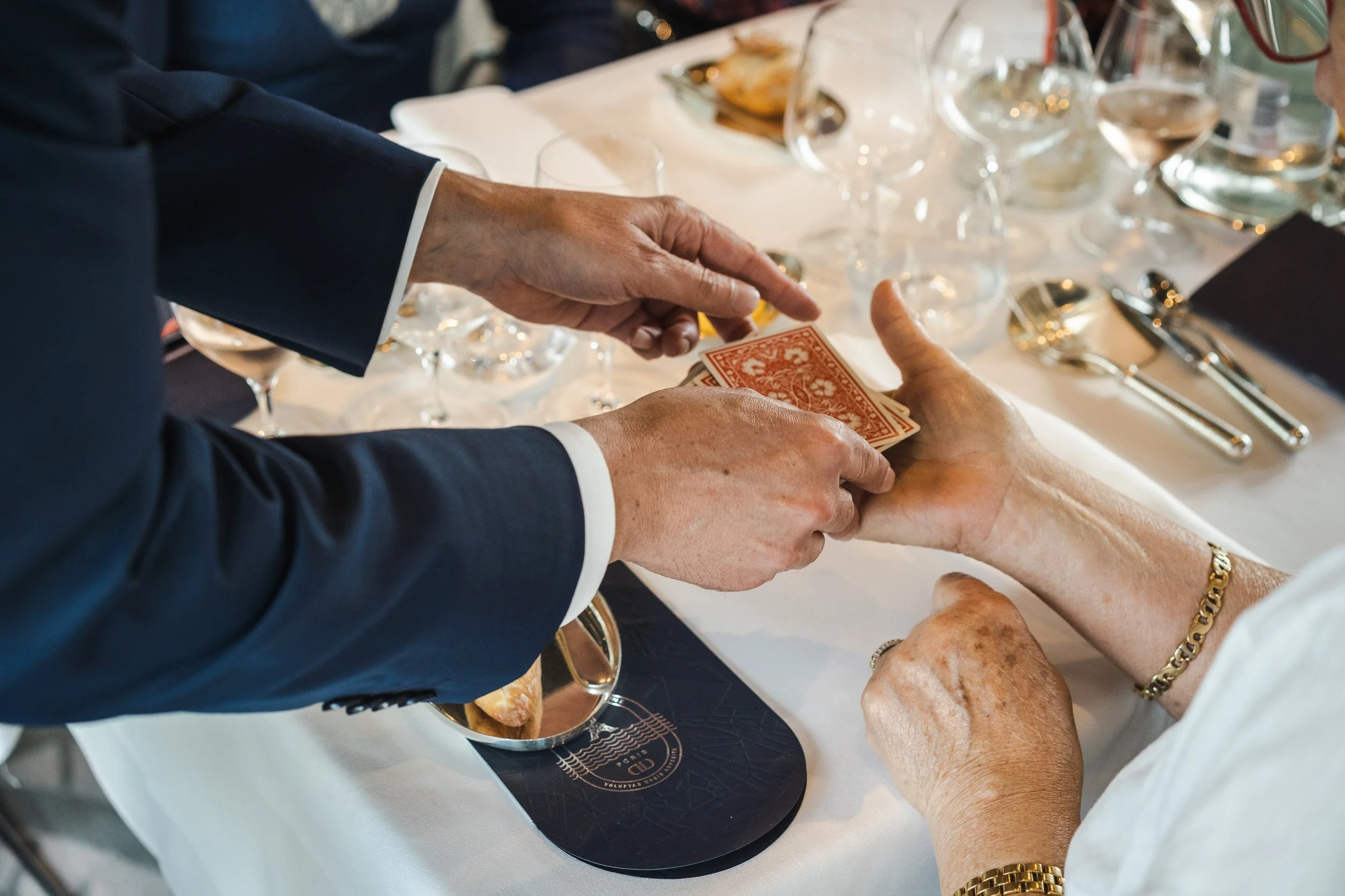 Une personne en costume échange de l'argent en papier avec une autre personne lors d'un repas dans un restaurant, autour d'une table avec des verres et des assiettes.