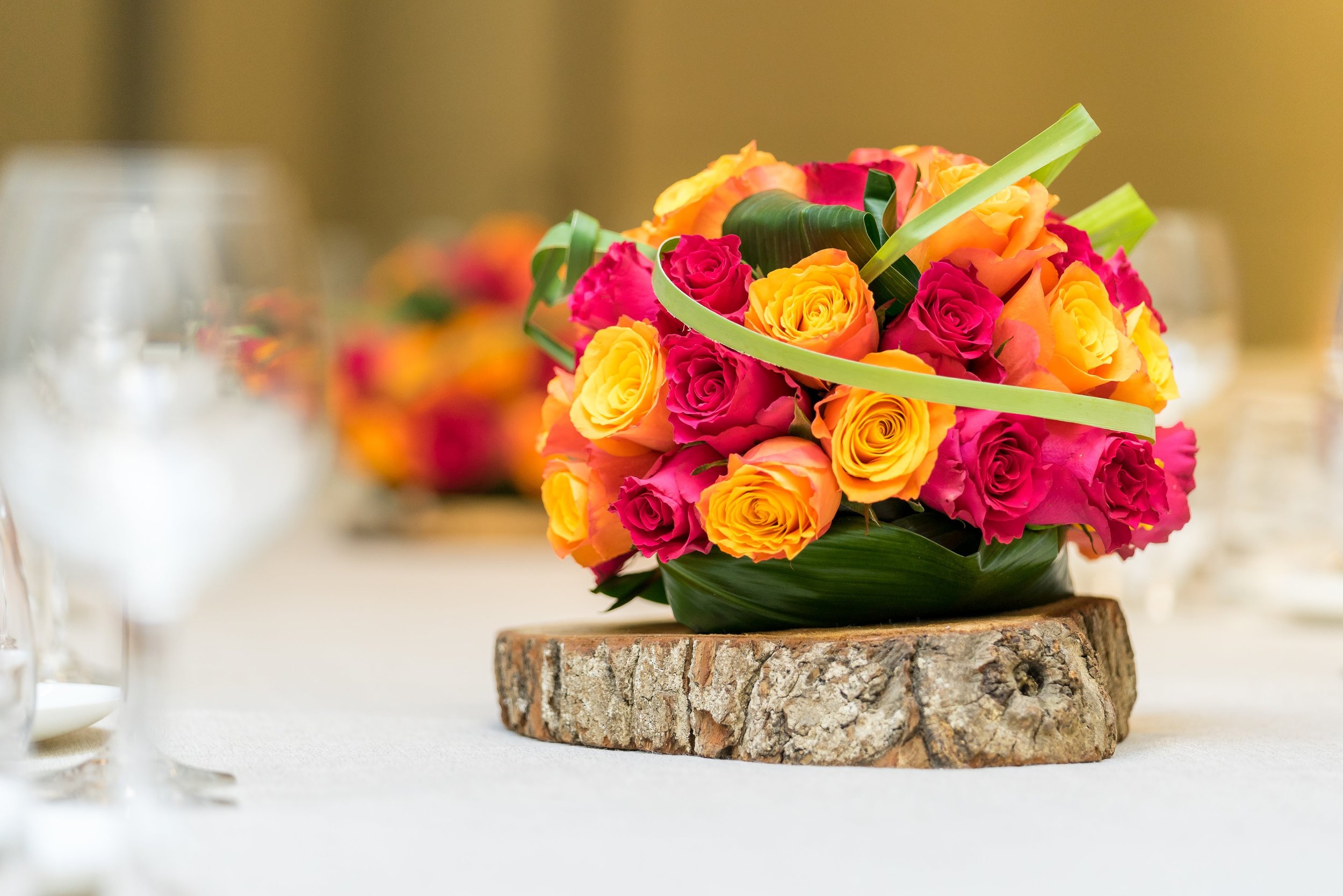 Bouquet de roses roses, oranges et jaunes sur une table en bois, décoré de ruban vert, avec un fond flou.