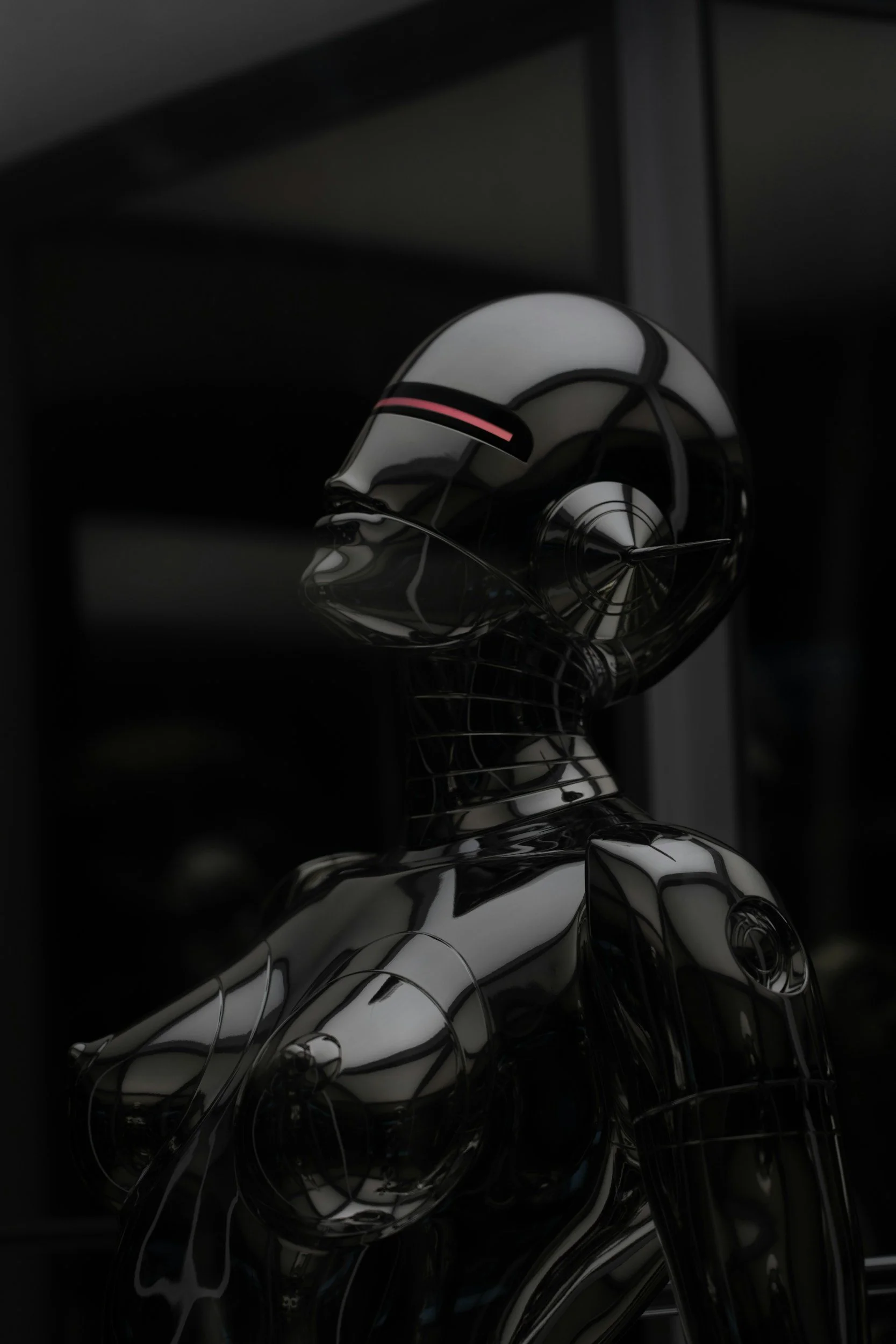 A shiny, reflective metallic sculpture of a human head and torso, with intricate lines and smooth curves, against a dark background.