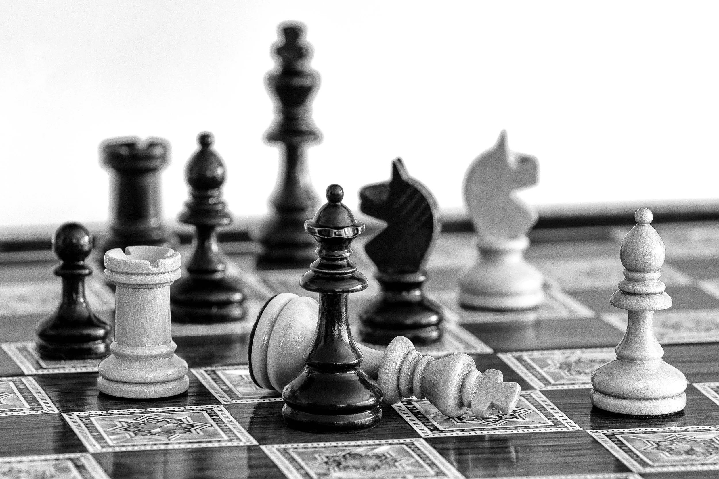 A chessboard with several chess pieces, including pawns, knights, bishops, and a king, in mid-game position in black and white