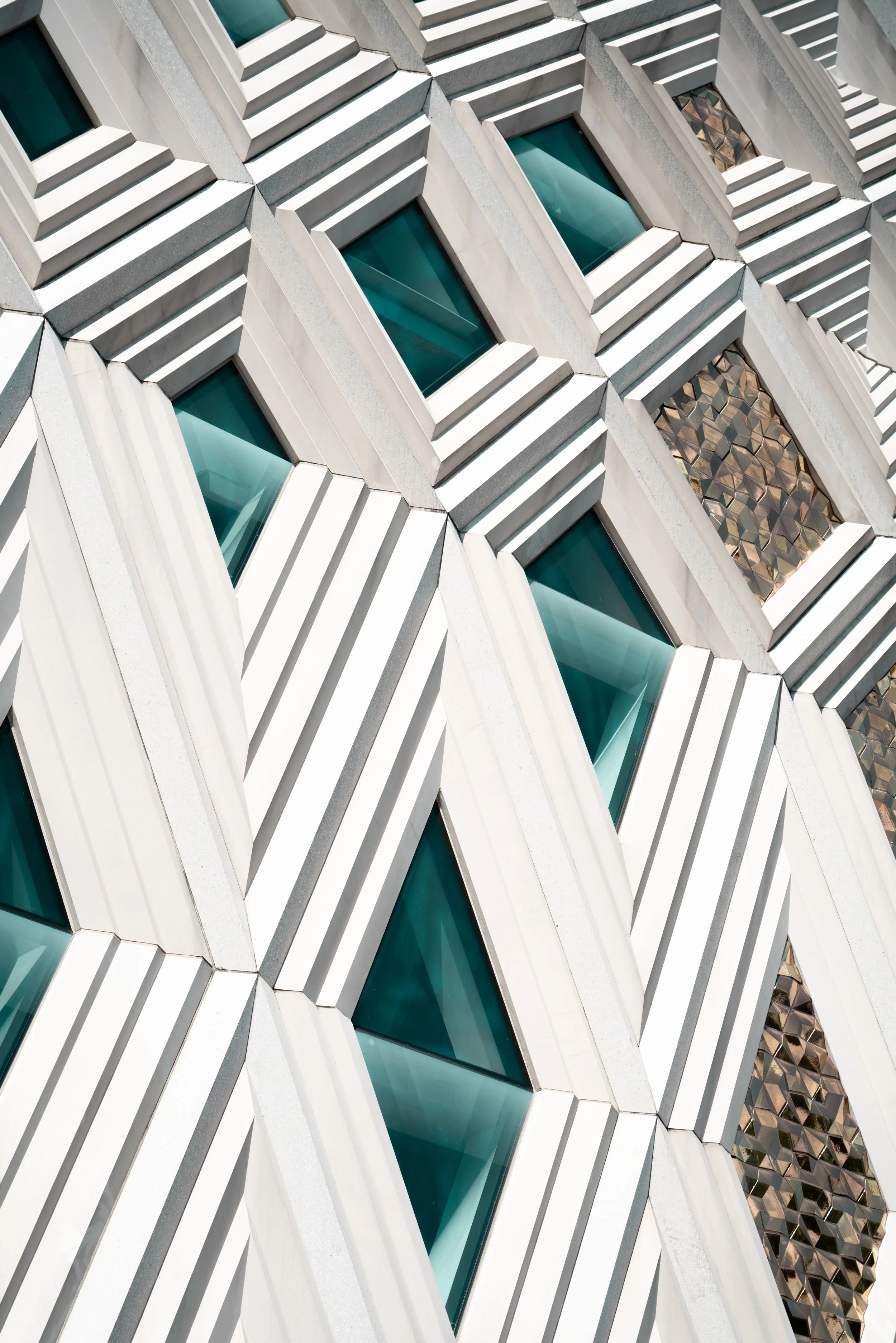 Close-up of a modern building facade with geometric patterned windows and layered architectural details in white and metallic tones.