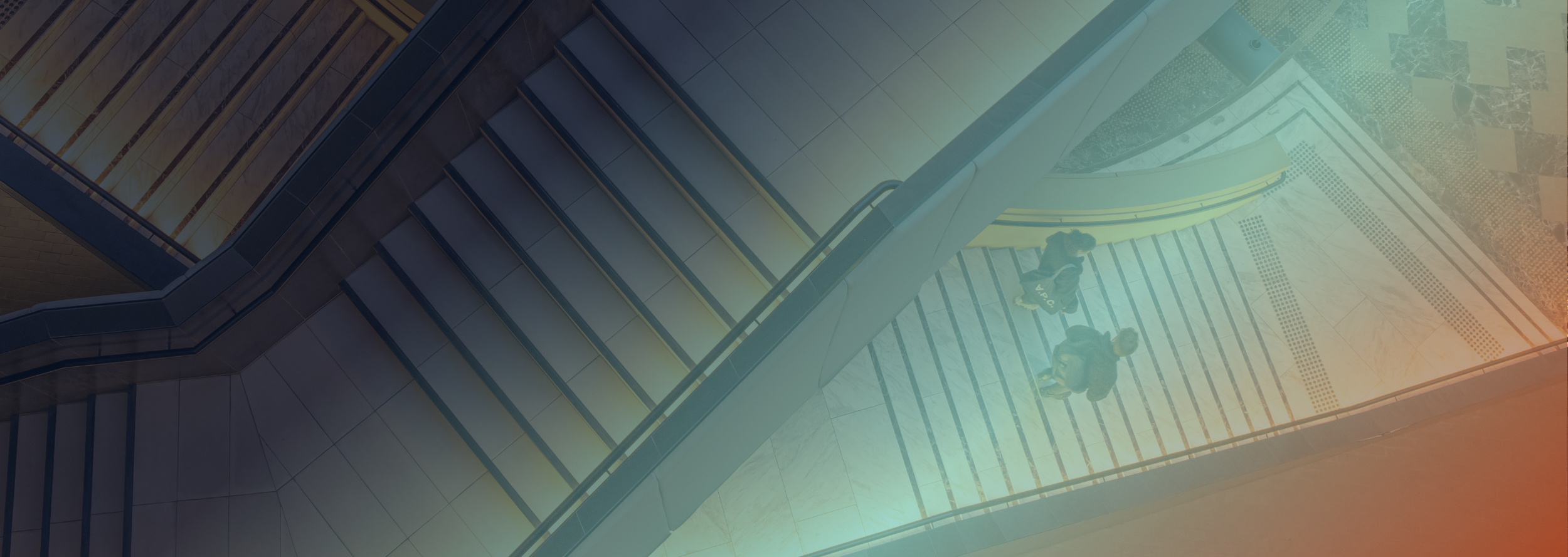 Two people walking on a staircase inside a modern building with glass and metal railings.