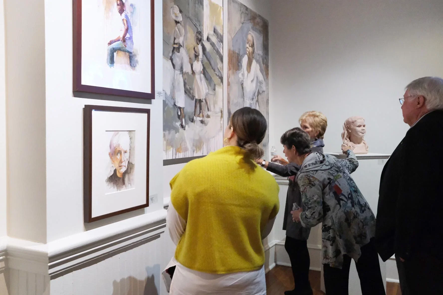 People viewing abstract and portrait paintings in an art gallery.