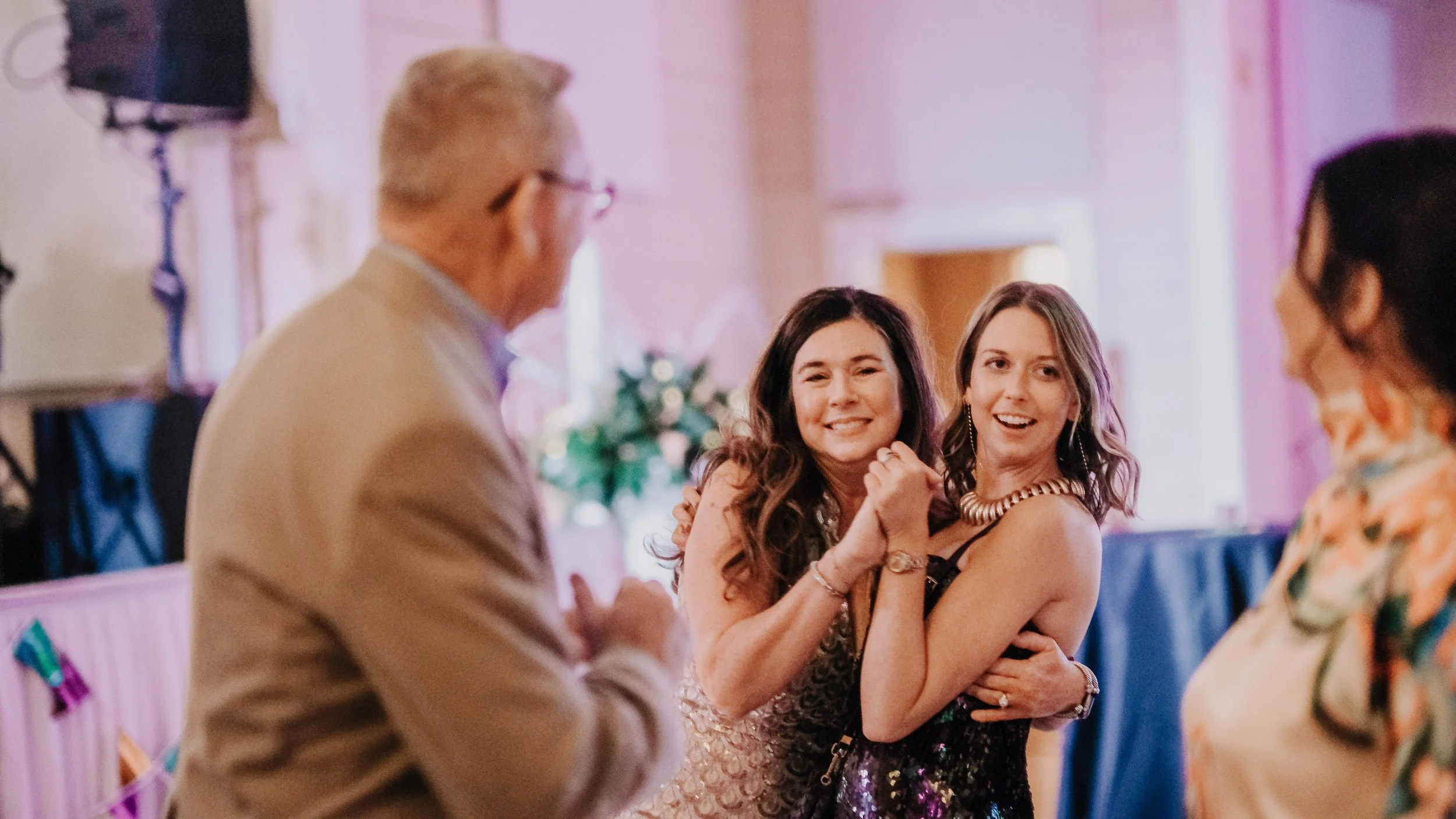 A group of four people at a celebration, smiling and interacting, with vibrant pink and purple decorations in the background.