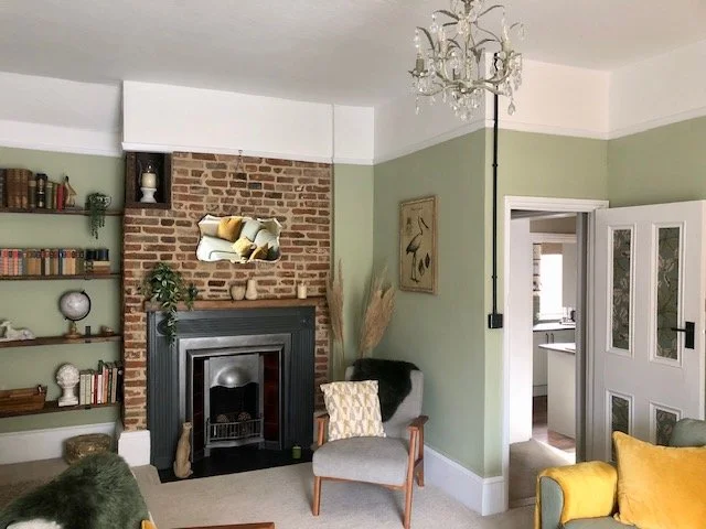 Living room with green walls, brick fireplace, built-in bookshelf, and a chandelier ceiling light.