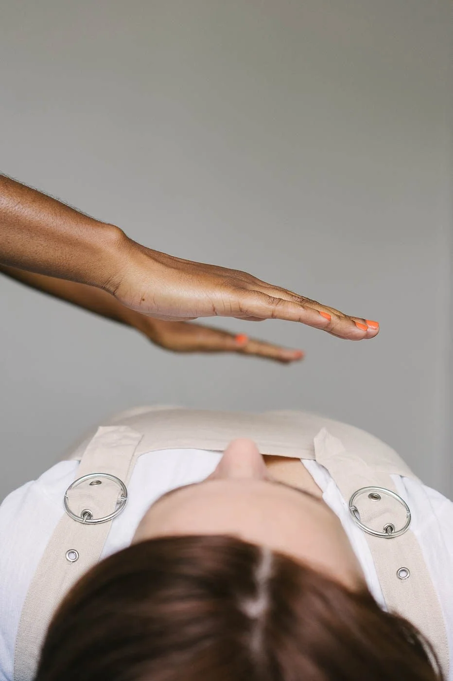 A person lying down with a harness around their shoulders and an outstretched hand above them.