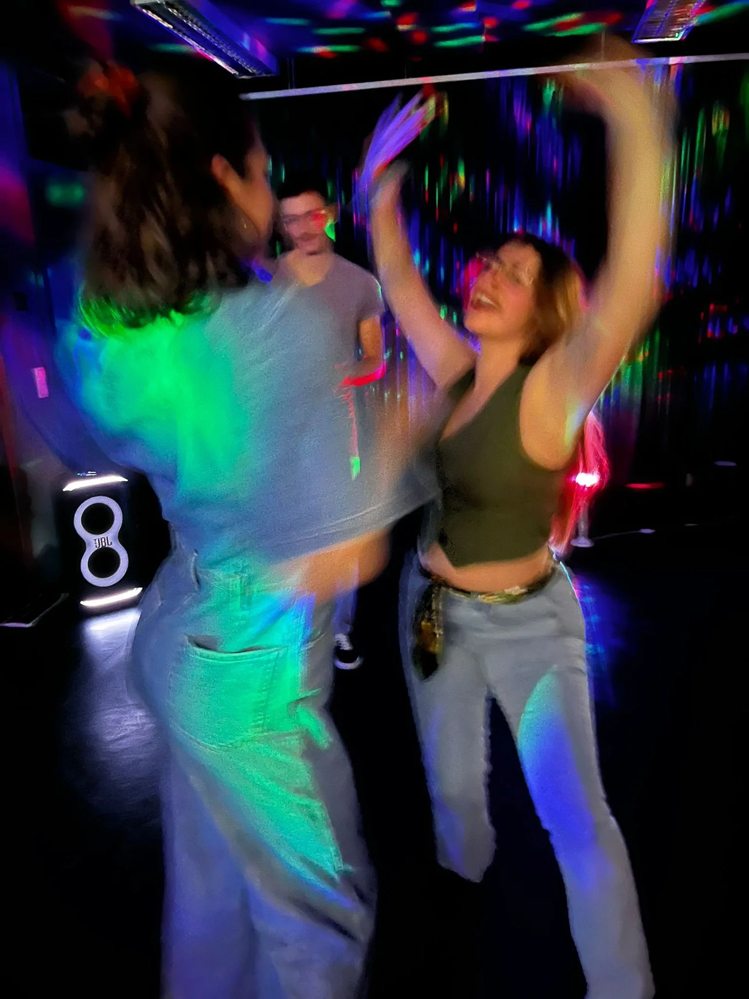 People dancing in a dark room with colorful lights and disco effects.