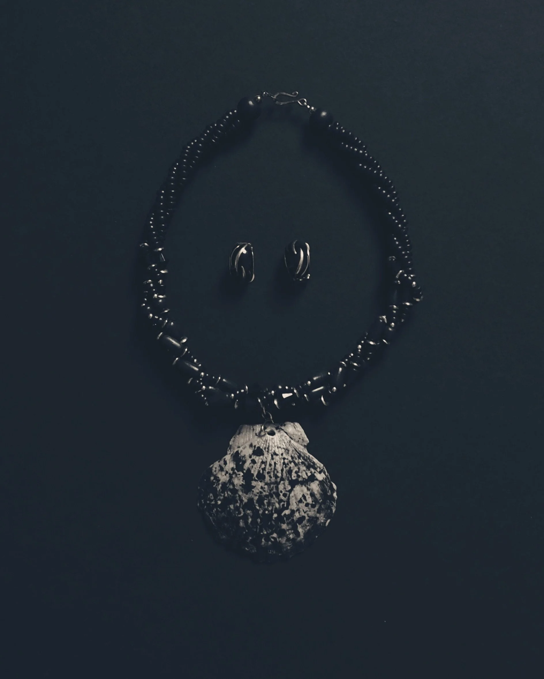 Schmuck aus schwarzem Metall mit einer Halskette, einem Paar Ohrringen, einem Anhänger und einem weiteren dekorativen Element, alle auf schwarzem Hintergrund.
