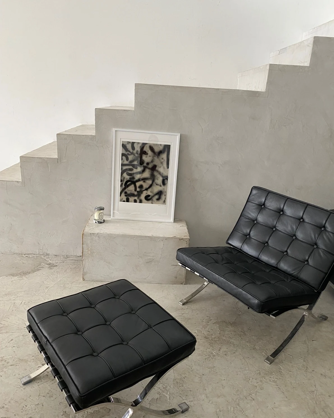 Modernes Wohnzimmer mit schwarzen Ledersesseln, einem gestreiften Kissen, einer weißen Wand, einer Treppe, einem stilvollen Rahmen mit abstrakter Kunst und einem kleinen Glas