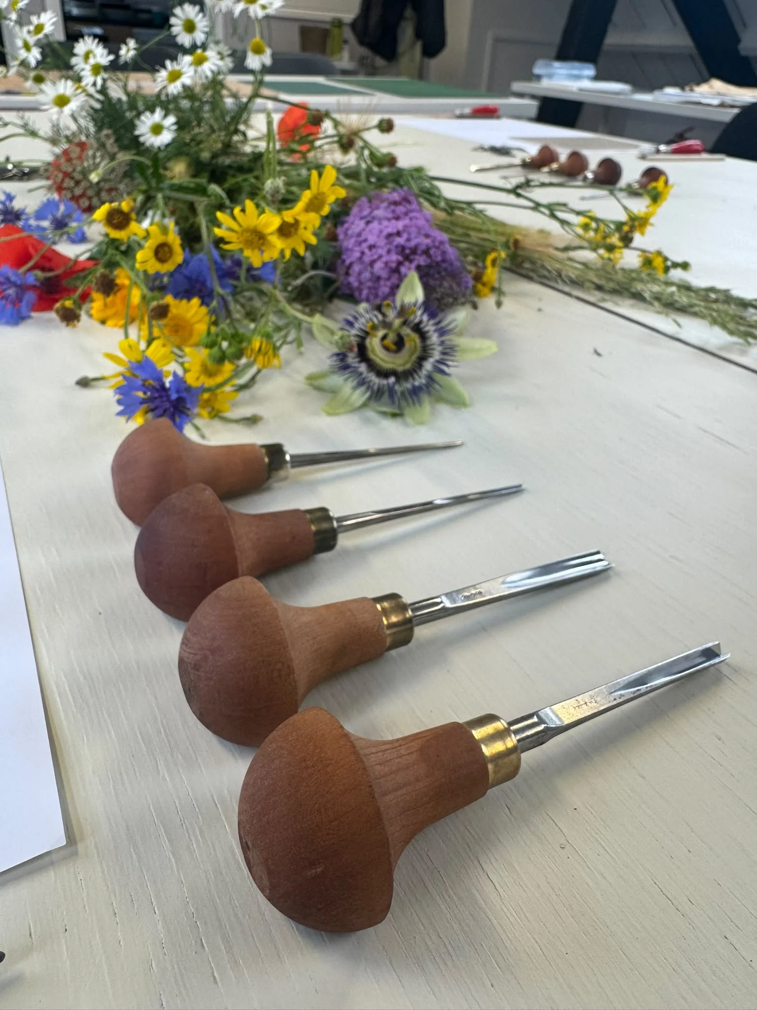 A set of woodworking carving tools with wooden handles includes various chisels and gouges laid out on a white wooden surface.