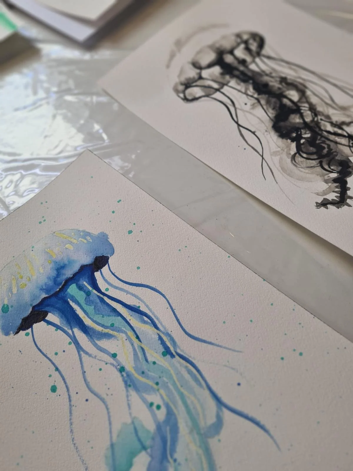 Watercolor paintings of jellyfish on white paper, featuring blue and black ink designs.
