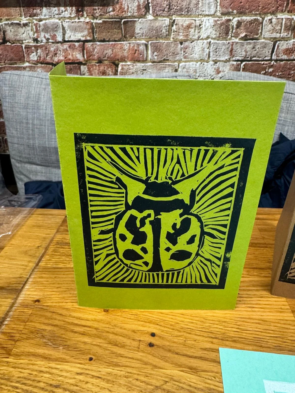 Green card with a black illustration of a ladybug on the front, featuring a detailed, stylized design with radiating lines in the background.