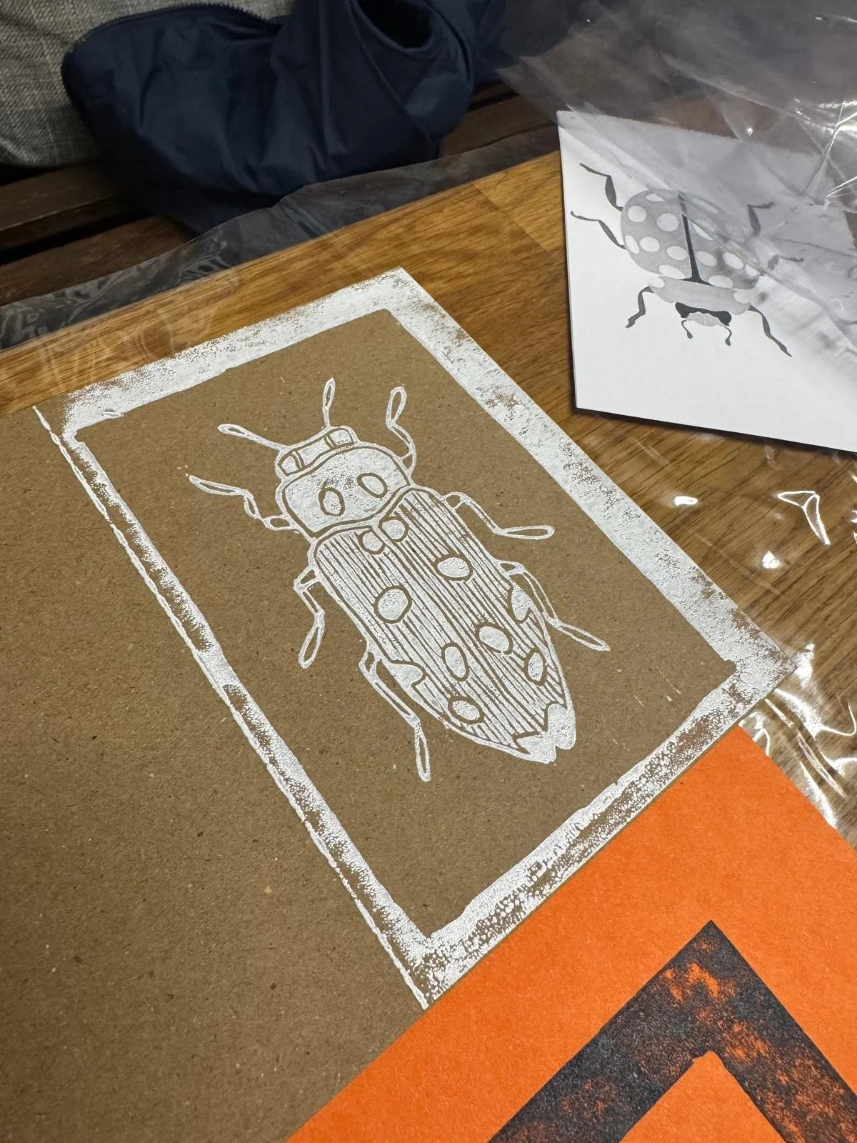 A white illustration of a ladybug on brown paper, with a similar ladybug drawing on white paper nearby.