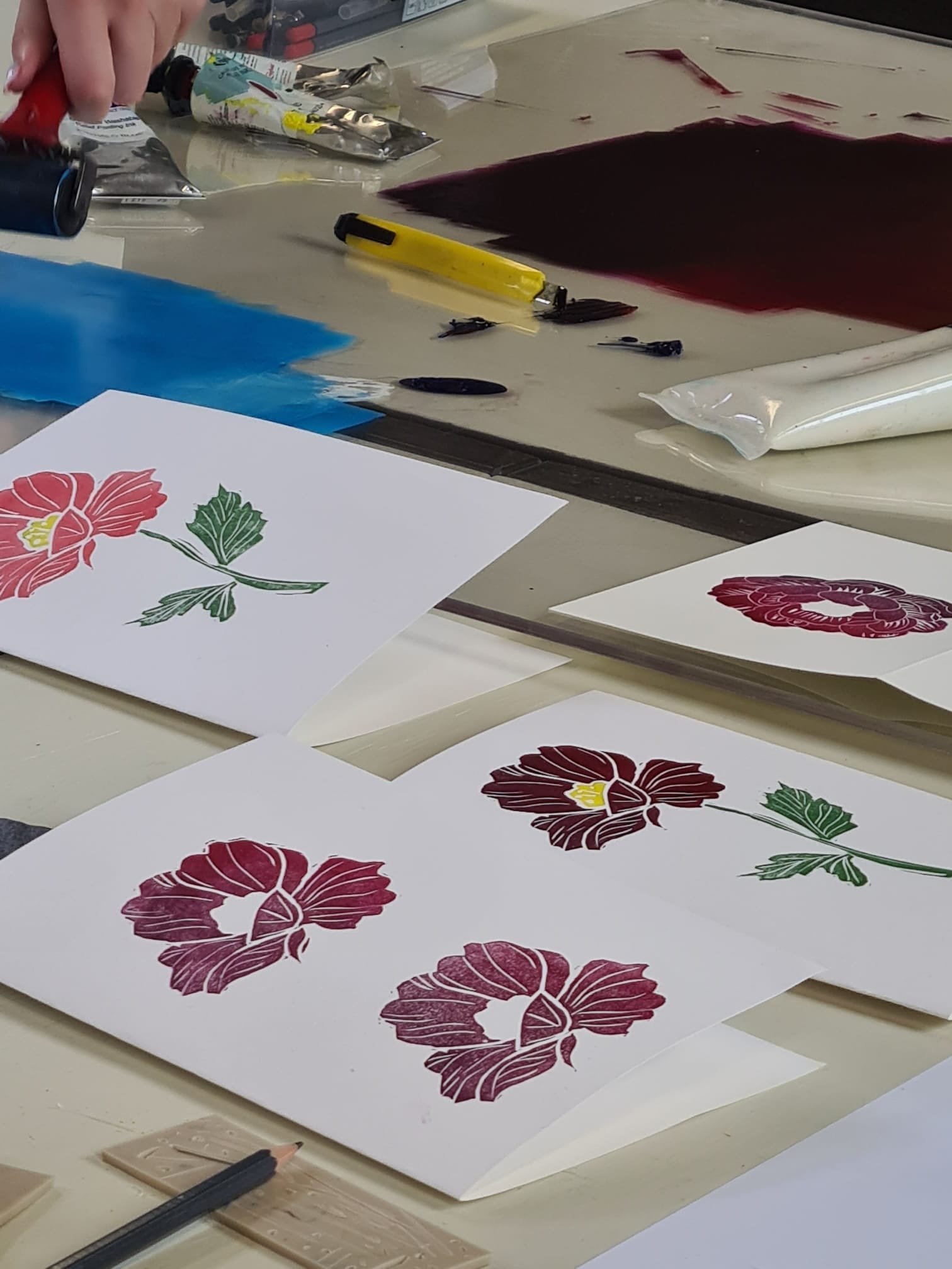 Sheets of paper with red and pink floral designs, indicating a traditional Japanese textile dyeing process, along with tools and materials on a table.
