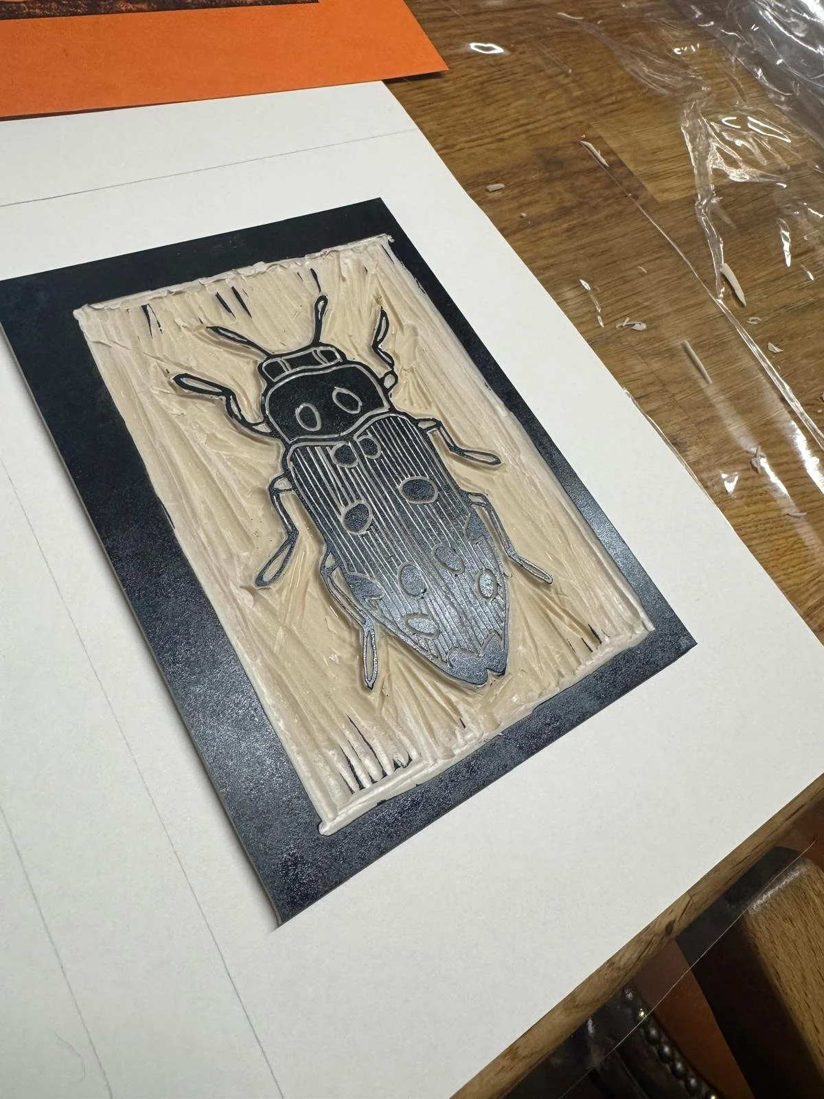 A detailed metallic print of a ladybird insect on a textured background, placed on a piece of white paper on a wooden table.