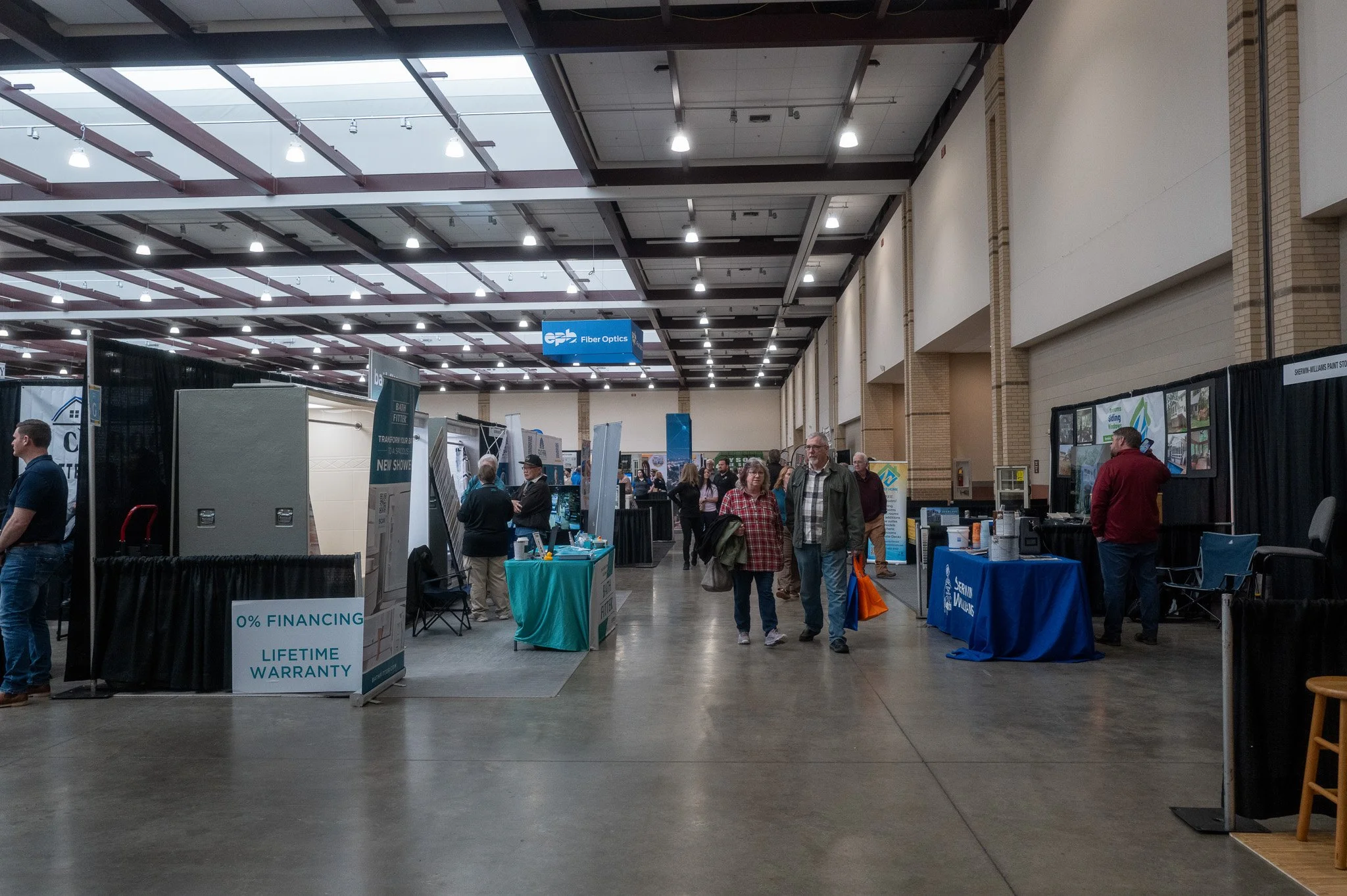 Indoor exhibition or trade show with multiple booths, people walking around, and signs promoting warranties and financing options.