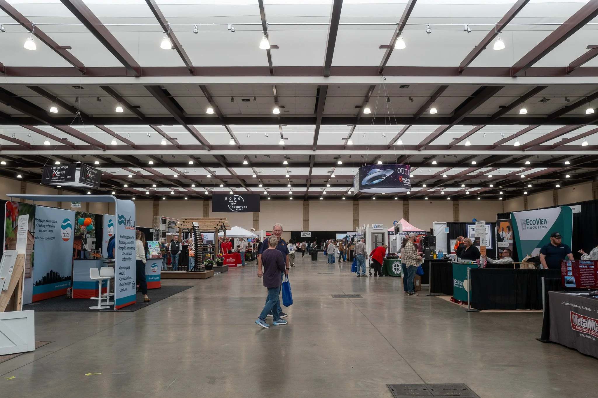 Indoor exhibition hall with booths, banners, and people walking around, part of a trade fair or convention.