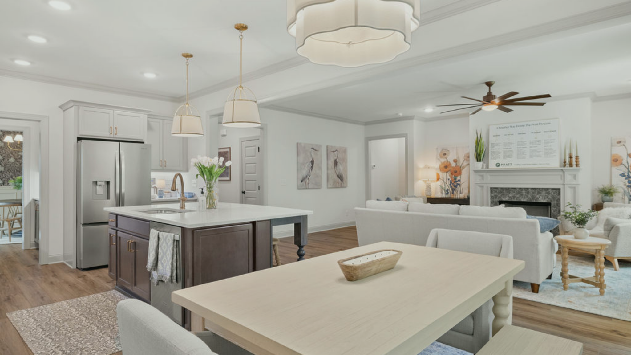 Open-concept living room and kitchen with white walls, pendant lighting, artwork, ceiling fan, and cozy seating area.