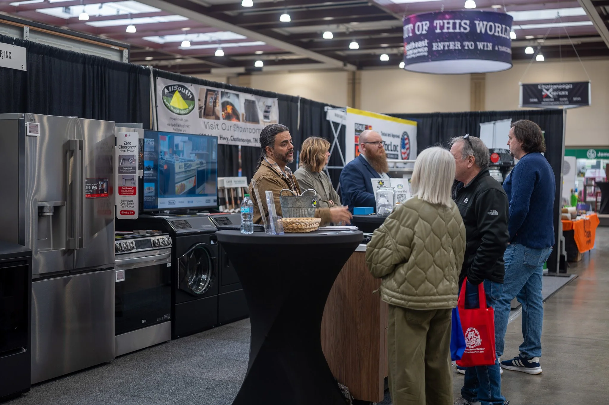People browsing at an indoor home appliance trade show with kitchen appliances and banners in the background.