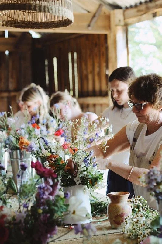 Women and children arranging flowers in a rustic wooden barn.