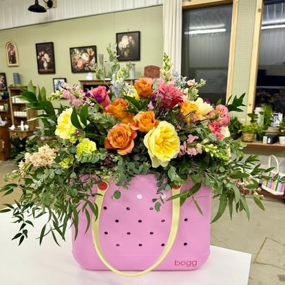 Flower arrangement in a pink basket with yellow, orange, pink, and purple flowers and greenery inside a shop.
