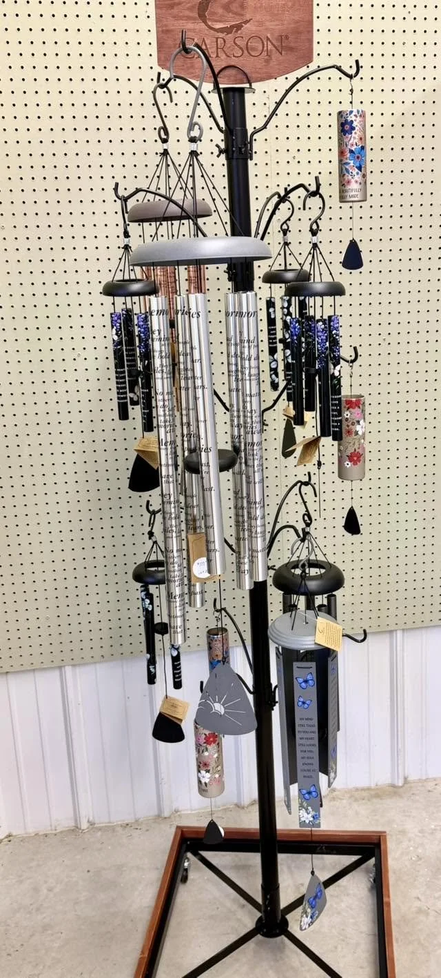 A metal display stand holding wind chimes of various styles and colors, set against a pegboard wall.