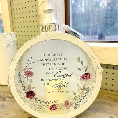 Decorative round glass clock with floral design and inspirational quote, placed on a wooden surface near a window.