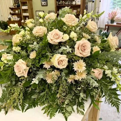 A large floral arrangement with light pink roses, white daisies, and green foliage.