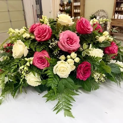 A floral arrangement with pink and white roses, surrounded by green leaves, on a white table in a floral shop.